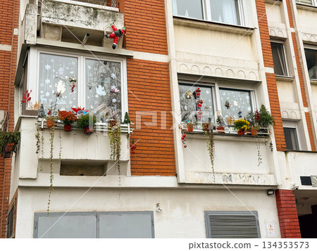 Apartment building facade with christmas decorated windows and balconies in winter city. Urban holiday decoration, residential tradition, cozy seasonal atmosphere and everyday festive celebration 134353573