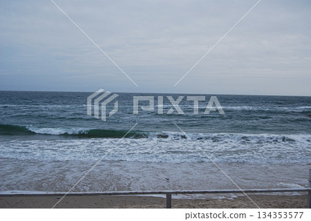 Sea waves crashing on a sandy shore under a cloudy sky. Waves crashing on a sandy shore under a cloudy sky, as seen from the railing on a beach in Odessa. Sea waves crashing on a sandy shore under a cloudy sky. Waves crashing on a sandy shore under a cloudy sky, as seen from the railing on a beach in Odessa. 134353577