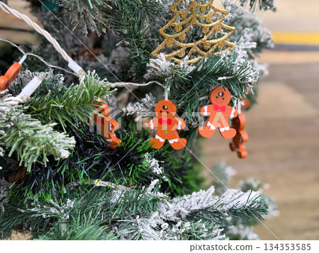 Gingerbread ornaments hanging on frosted Christmas tree branches. Playful holiday decor, winter detail and festive seasonal mood Gingerbread ornaments hanging on frosted Christmas tree branches. Playful holiday decor, winter detail and festive seasonal mood 134353585