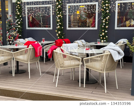 Outdoor cafe terrace decorated for Christmas with blankets and lights. Winter leisure space, seasonal hospitality and festive urban atmosphere 134353596
