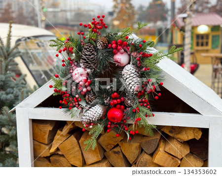 Christmas wreath with pine cones and red berries on firewood shed. Rustic winter decor, seasonal tradition and cozy outdoor atmosphere 134353602