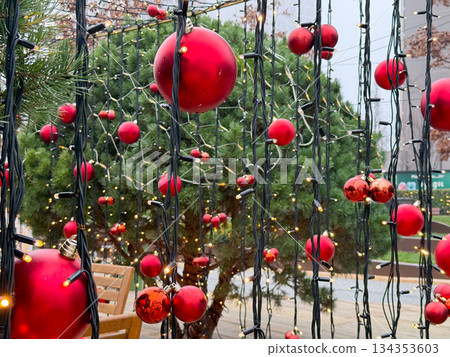 Red Christmas baubles hanging on string lights in outdoor setting. Festive urban decor, winter atmosphere and seasonal holiday illumination Red Christmas baubles hanging on string lights in outdoor setting. Festive urban decor, winter atmosphere and seasonal holiday illumination 134353603