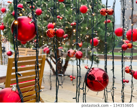 Red Christmas baubles hanging on string lights in outdoor setting. Festive urban decor, winter atmosphere and seasonal holiday illumination Red Christmas baubles hanging on string lights in outdoor setting. Festive urban decor, winter atmosphere and seasonal holiday illumination 134353605