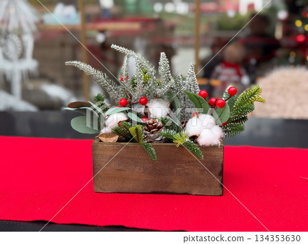 Christmas floral arrangement in wooden box on red tablecloth. Festive decor composition, holiday centerpiece and seasonal styling 134353630