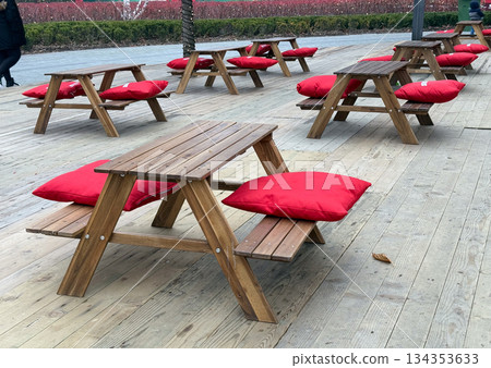 Wooden picnic tables with red cushions on outdoor winter terrace. Public seating, urban leisure space and seasonal open air cafe area Wooden picnic tables with red cushions on outdoor winter terrace. Public seating, urban leisure space and seasonal open air cafe area 134353633