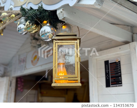 Vintage lantern glowing under decorated Christmas market roof. Warm festive lighting, winter holiday mood and cozy seasonal street atmosphere. 134353670