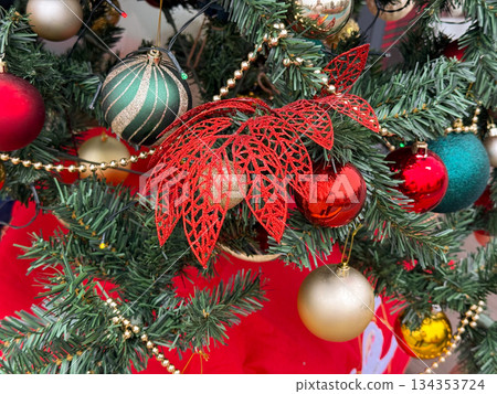 Decorative red lace bow among Christmas ornaments on fir tree branch. Festive detail, winter decor, traditional holiday symbolism and seasonal design. 134353724