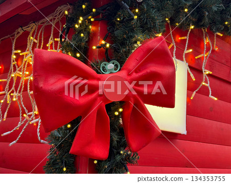 Large red Christmas bow decoration on festive wooden background with lights. Holiday decor detail, seasonal design, winter celebration and cheerful traditional atmosphere. Large red Christmas bow decoration on festive wooden background with lights. Holiday decor detail, seasonal design, winter celebration and cheerful traditional atmosphere. 134353755
