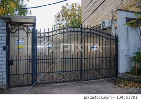 Ornate wrought iron gate entrance to a property. Ornate wrought iron gate features intricate scroll patterns and spearhead finials.  134353791
