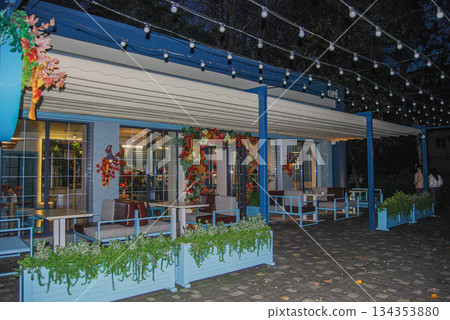 Cozy outdoor restaurant patio at night with string lights and autumn decor. Outdoor restaurant patio at night featuring overhanging string lights casting a warm glow. Cozy outdoor restaurant patio at night with string lights and autumn decor. Outdoor restaurant patio at night featuring overhanging string lights casting a warm glow. 134353880