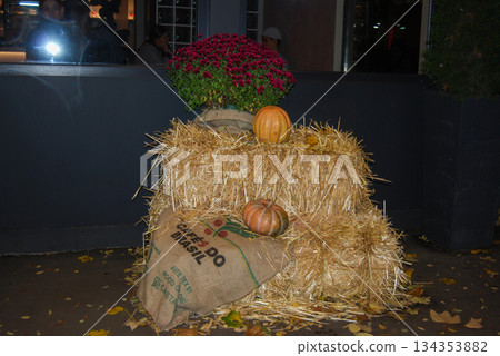 Autumn harvest display with pumpkins, hay bales, and chrysanthemums. Hay bales stacked in front of a dark wall form the centerpiece of an autumn display. Autumn harvest display with pumpkins, hay bales, and chrysanthemums. Hay bales stacked in front of a dark wall form the centerpiece of an autumn display. 134353882