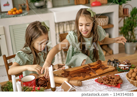 The girls are having fun making Christmas gingerbread cookies from chocolate dough in the kitchen decorated for the winter holidays The girls are having fun making Christmas gingerbread cookies from chocolate dough in the kitchen decorated for the winter holidays 134354085