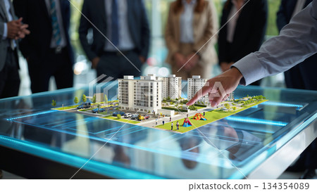 Futuristic Real Estate Project Presentation. A group of professionals gathers around an illuminated table displaying a detailed scale model of a modern real estate development. Futuristic Real Estate Project Presentation. A group of professionals gathers around an illuminated table displaying a detailed scale model of a modern real estate development. 134354089