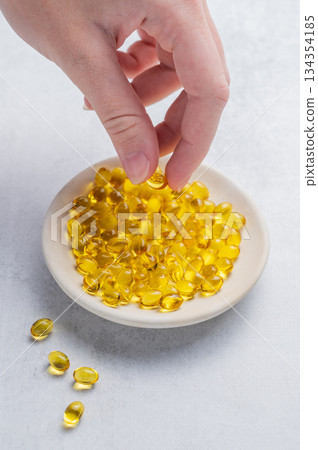 A hand holding a soft capsule containing D3 in a plate on a light background. A hand holding a soft capsule containing D3 in a plate on a light background. 134354185