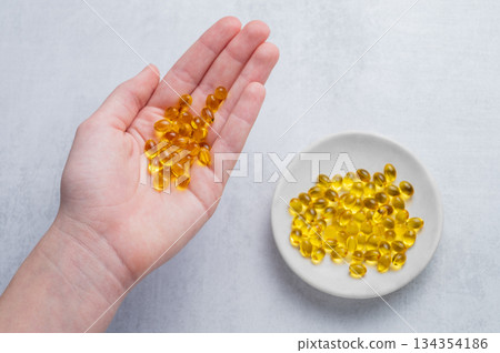 A hand holding a soft capsules containing D3 on a light background. A hand holding a soft capsules containing D3 on a light background. 134354186