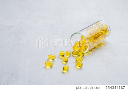 Yellow softgel vitamins capsules scattered in a bottle on a light background. Yellow softgel vitamins capsules scattered in a bottle on a light background. 134354187