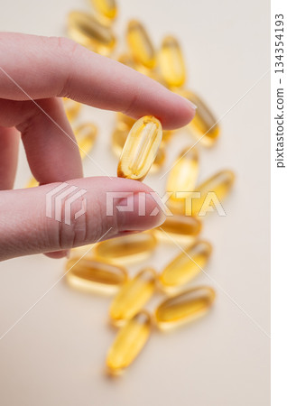 A hand holding a soft capsule containing Omega on a yellow background. A hand holding a soft capsule containing Omega on a yellow background. 134354193