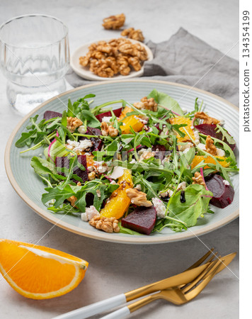 A fresh salad of beets, orange, and arugula with feta, walnuts, and balsamic dressing on a plate 134354199
