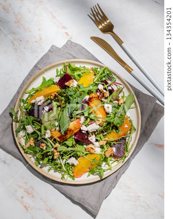 A fresh salad of beets, orange, and arugula with feta, walnuts, and balsamic dressing on a plate 134354201