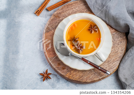 Sea buckthorn herbal tea in a cup on a wooden board on a light background with spices 134354206