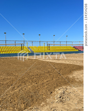 Empty beach volleyball court with colorful stadium seats under clear blue sky. 134354208