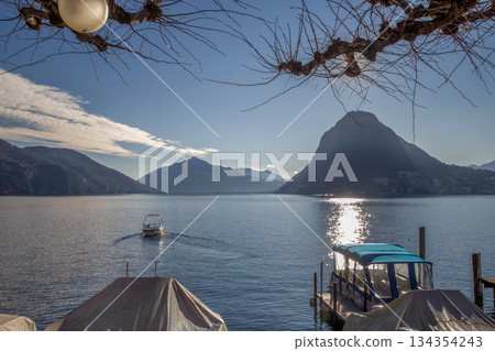 Small harbor and motorboat moving to coastline on Lake Lugano or Lake Geneva Small harbor and motorboat moving to coastline on Lake Lugano or Lake Geneva 134354243