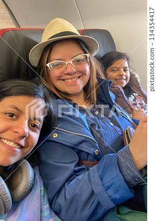 Three women are sitting on a plane, smiling and posing for a picture 134354417