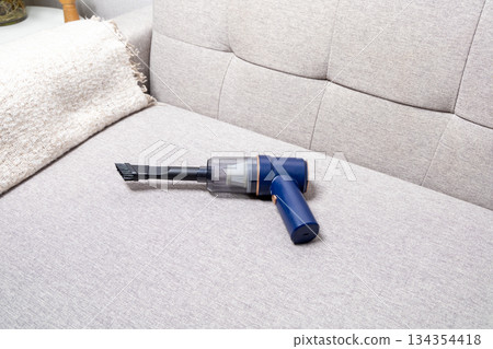 A blue vacuum cleaner is on a couch 134354418
