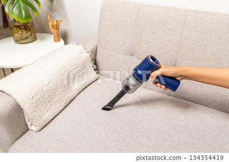 A person is vacuuming a couch with a blue vacuum cleaner 134354419