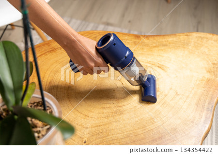 A person is cleaning a wooden table with a vacuum cleaner 134354422