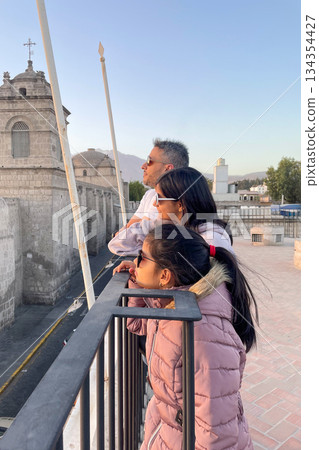 A family of three people are standing on a balcony looking out over a city 134354427