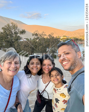 A family of five is posing for a photo on a Huacachina Oasis. Peru A family of five is posing for a photo on a Huacachina Oasis. Peru 134354434