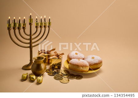 Hanukkah Celebration Setup. A menorah, dreidels, gift boxes, and donuts on a beige background Hanukkah Celebration Setup. A menorah, dreidels, gift boxes, and donuts on a beige background 134354495