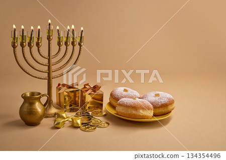 Hanukkah Celebration Setup. A menorah, dreidels, gift boxes, and donuts on a beige background 134354496