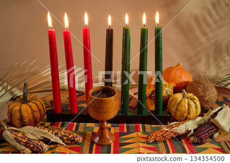 Kwanzaa Celebration Setup. A vibrant Kwanzaa display with colorful candles, fruits, corn, and a wooden chalice Kwanzaa Celebration Setup. A vibrant Kwanzaa display with colorful candles, fruits, corn, and a wooden chalice 134354500