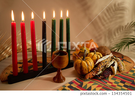 Kwanzaa Celebration Setting. Warm Kwanzaa scene with lit candles, harvest vegetables, and a wooden chalice Kwanzaa Celebration Setting. Warm Kwanzaa scene with lit candles, harvest vegetables, and a wooden chalice 134354501