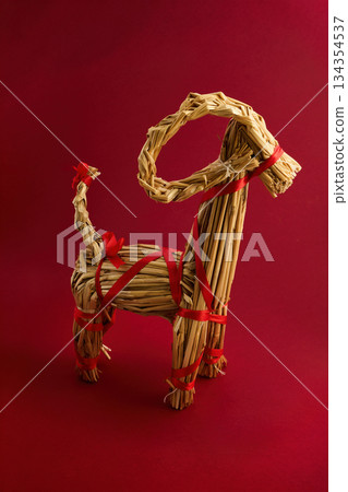 Straw Goat Sculpture. A straw goat sculpture with red ribbons against a red backdrop. Straw Goat Sculpture. A straw goat sculpture with red ribbons against a red backdrop. 134354537