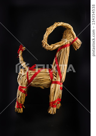 Straw Goat Sculpture. A handcrafted straw goat with red ribbon accents on a dark background. 134354538