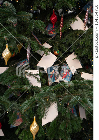 Christmas tree decorated with blank paper tags and festive ornaments, green pine branches and warm lights creating a cozy holiday mood 134354710