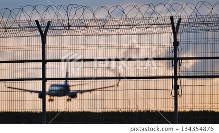 Airplane landing behind airport fence at sunset representing travel restrictions 134354876