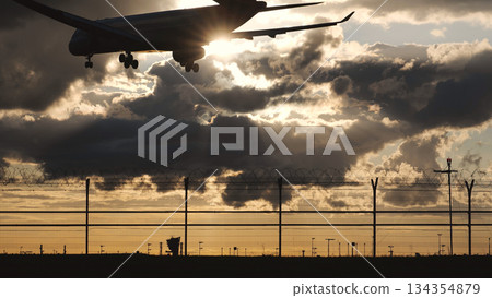 Airplane landing at sunset, silhouette against dramatic sky over airport fence 134354879