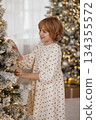 Side view of Caucasian blonde girl decorating Christmas tree in cozy room 134355572
