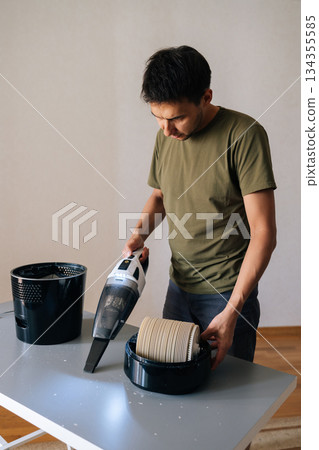 Vertical portrait of man cleaning table with air humidifier using small vacuum cleaner, demonstrating home appliance maintenance for improved air quality and hygiene. Concept of household chores. Vertical portrait of man cleaning table with air humidifier using small vacuum cleaner, demonstrating home appliance maintenance for improved air quality and hygiene. Concept of household chores. 134355585