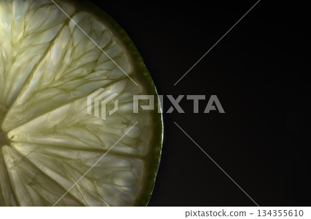 Shimmering lime segment radiates freshness against shadowy background Shimmering lime segment radiates freshness against shadowy background 134355610