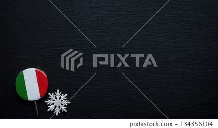 An Italian flag pin and a white snowflake decoration rest on a dark textured background, offering ample copy space for seasonal or national themes. 134356104