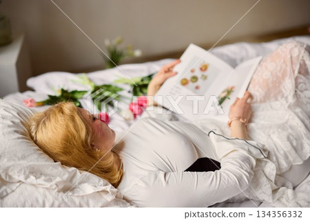Morning Serenity As Woman Leisurely Studies Botanical Illustrations On Bright Sunlit Bedding 134356332