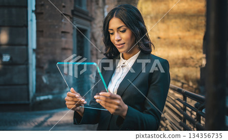 Businesswoman wearing suit using transparent digital tablet on city street 134356735