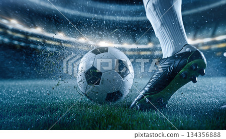 Soccer player kicks ball on field during match in stadium at night with lights shining brightly 134356888