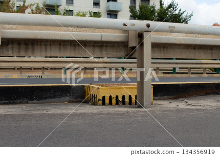 Concrete divider on a busy roadway with a drainage grate in an urban setting Concrete divider on a busy roadway with a drainage grate in an urban setting 134356919