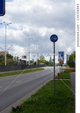 Bicycle lane alongside a broad road in a quiet urban area under a cloudy sky Bicycle lane alongside a broad road in a quiet urban area under a cloudy sky 134356943